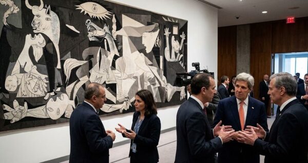 国連安全保障理事会の記者会見場。壁に掲げられたピカソの「ゲルニカ」のタペストリーの前で、何人かの外交官や記者が立ち話をしており、そのうちの一人が真剣な面持ちで絵を見上げている。